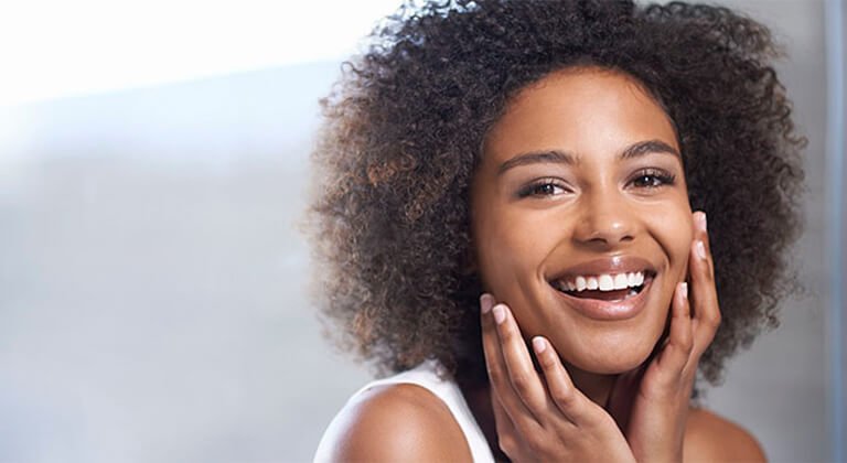 chica mulata con pelo afro sonriendo y tocándose la cara