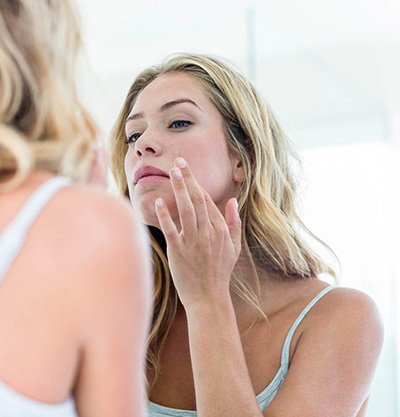 chica rubia mirando su reflejo en el espejo y quitándose un grano