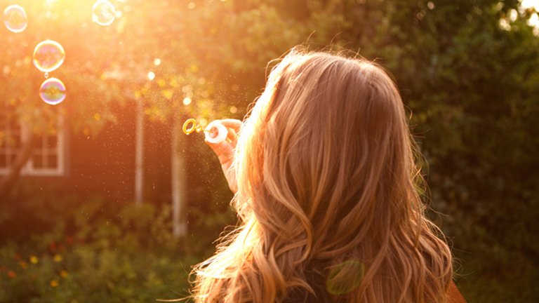 mujer pelo largo de espaldas haciendo pompas de jabón
