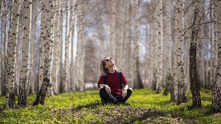 Chica sentada en medio de una arboleda mirando el cielo