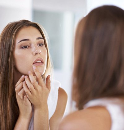 mujer quitándose granos frente al espejo