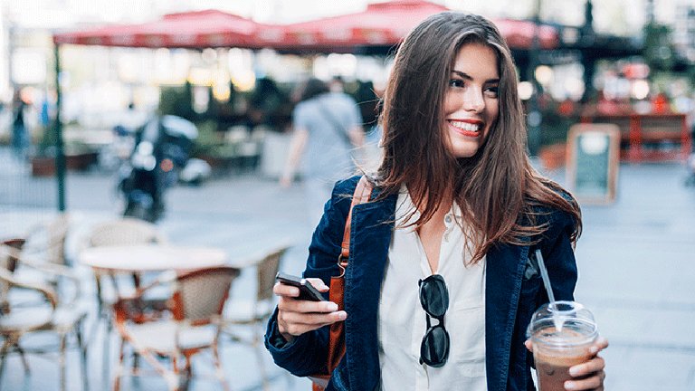 mujer en la calle con café y móvil en la mano