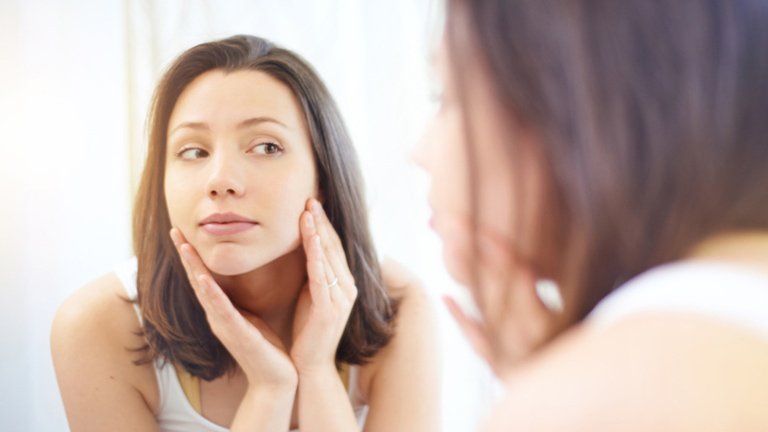 Mujer observándose el rostro en un espejo