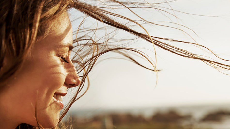 Rostro de mujer sonriendo con ojos cerrados y cabello al viento