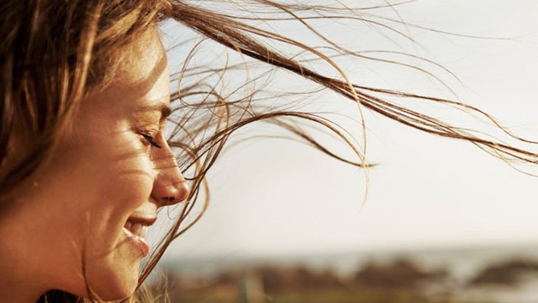Rostro de mujer sonriendo con ojos cerrados y cabello al viento