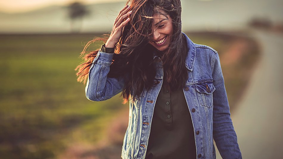Mujer sonriente paseando y apartándose la melena del rostro