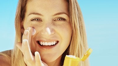 Mujer sonriente poniéndose crema en el rostro