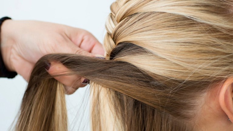 Mano realizando una trenza en cabello de mujer