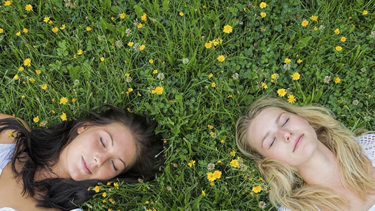 Dos mujeres tumbadas en el césped, una morena y otra rubia