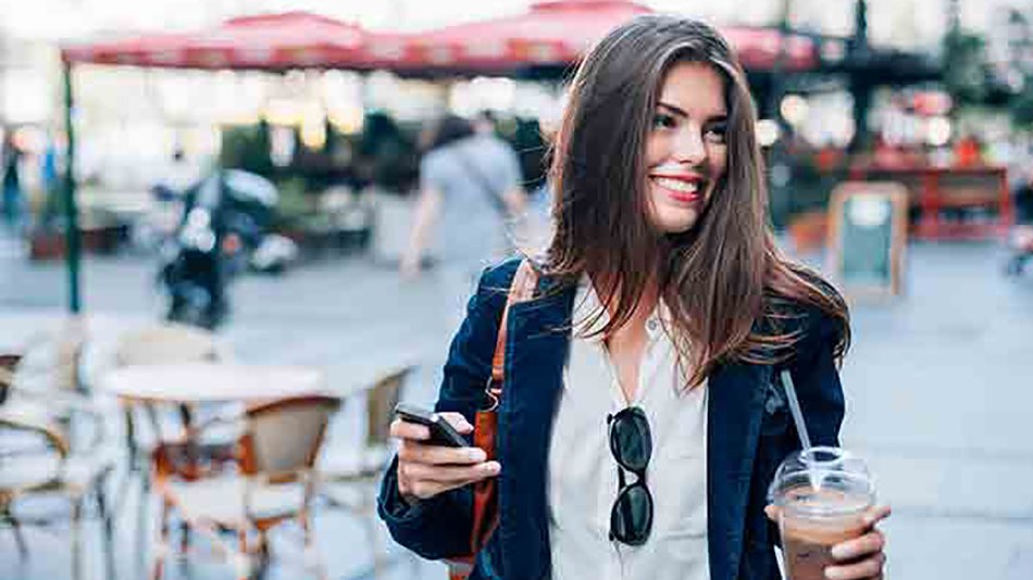 mujer sonriente paseando con bebida y móvil