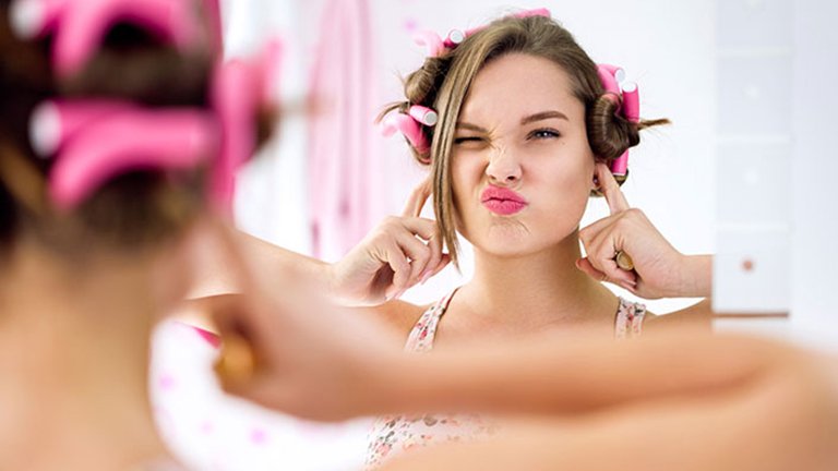 Mujer joven haciéndose un peinado divertido frente al espejo