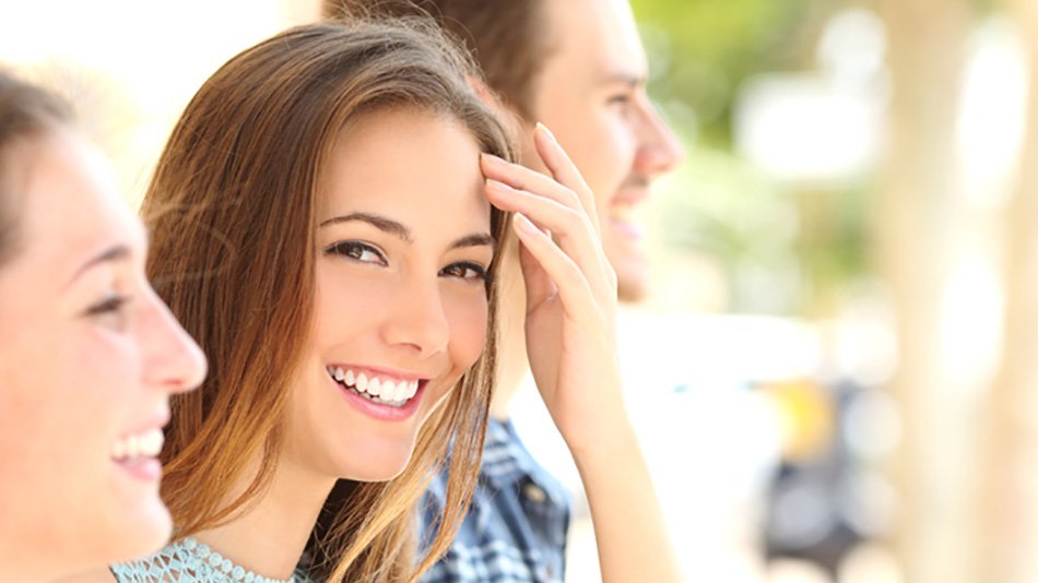 Chica mirando a camara y riendo junto a dos amigos