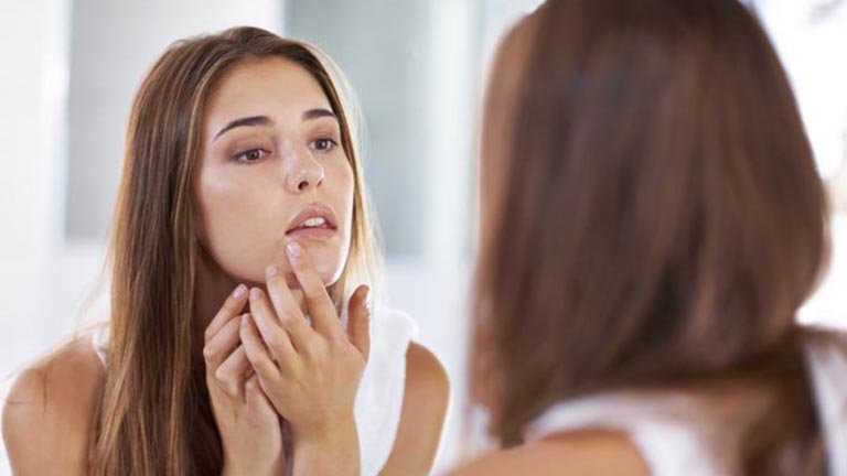 mujer tocándose la cara frente al espejo