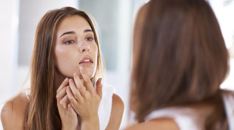 mujer tocándose la cara frente al espejo