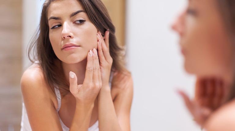 mujer morena mirándose al espejo y tocándose la cara