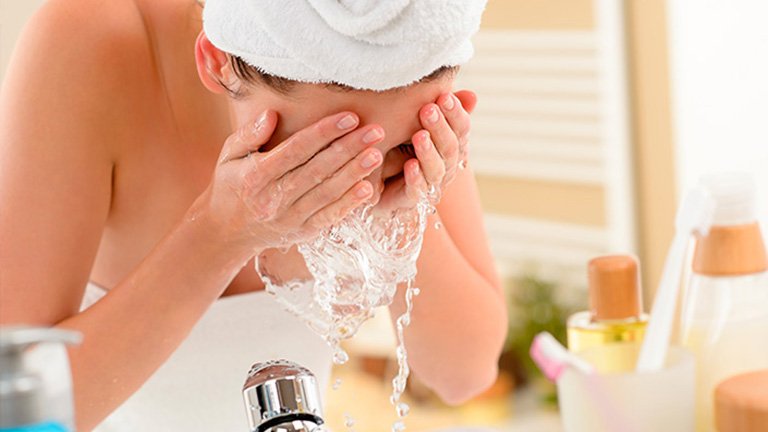 mujer lavándose la cara con agua