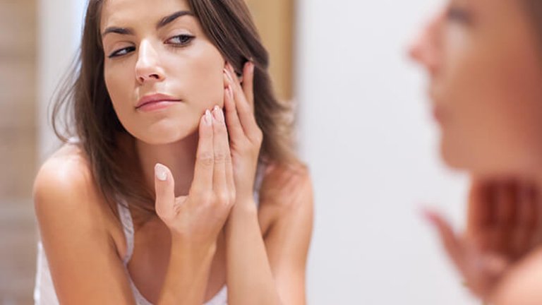 Mujer examinando su rostro frente al espejo