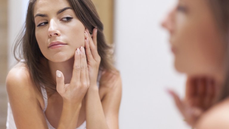 Mujer examinando su rostro frente al espejo